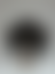 A male performer stands in a classic Kabuki pose within a bright, minimal space. He wears a wide black kimono jacket with subtle gold embroidery over a pale undergarment. His face is painted white with dark accents around the eyes and mouth — a modern, minimalist interpretation of traditional Kabuki makeup.