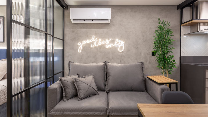 Foto de uma sala no estilo novaiorquino minimalista, com sofá, almofadas, letreiro em neon e uma planta de decoração.