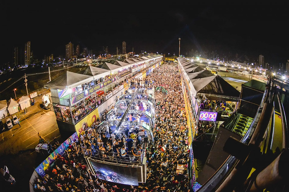 Multidão curtindo o Carnatal em Natal, com trios elétricos e camarotes iluminados ao fundo.