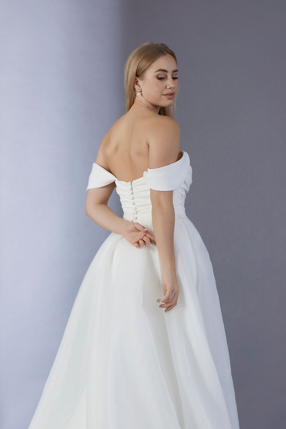 Thumbnail: A girl wearing a Luxury Crepe draped wedding dress with V-details neckline is showing her back and looking from her shoulder