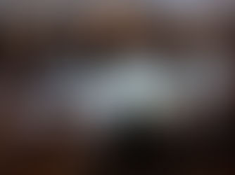 A wedding reception with guests sitting at round tables around an empty dance floor. The guests look bored, confused, and disengaged. Some are staring at their phones, others are chatting quietly without much energy. The lighting is dim, and the mood is dull. The room is decorated for a wedding with white tablecloths, floral centerpieces, and string lights, but the overall vibe feels awkward and lifeless.