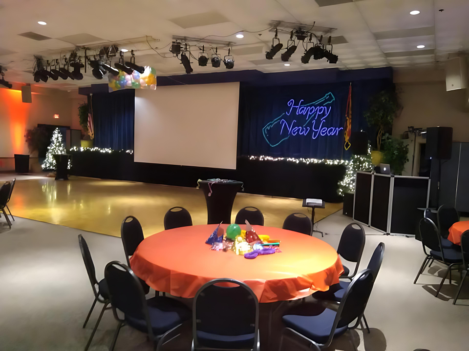 A festive New Year's celebration setup featuring orange tables, a decorated stage with "Happy New Ye