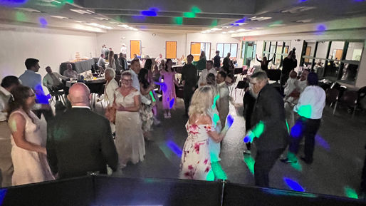 An independent Phoenix wedding DJ keeping the dance floor alive as dressed-up guests smile and dance together during an indoor wedding reception on a concrete floor.
