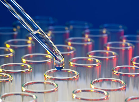 A closeup of a drop of liquid at the end of a pipette above a test tube in a group