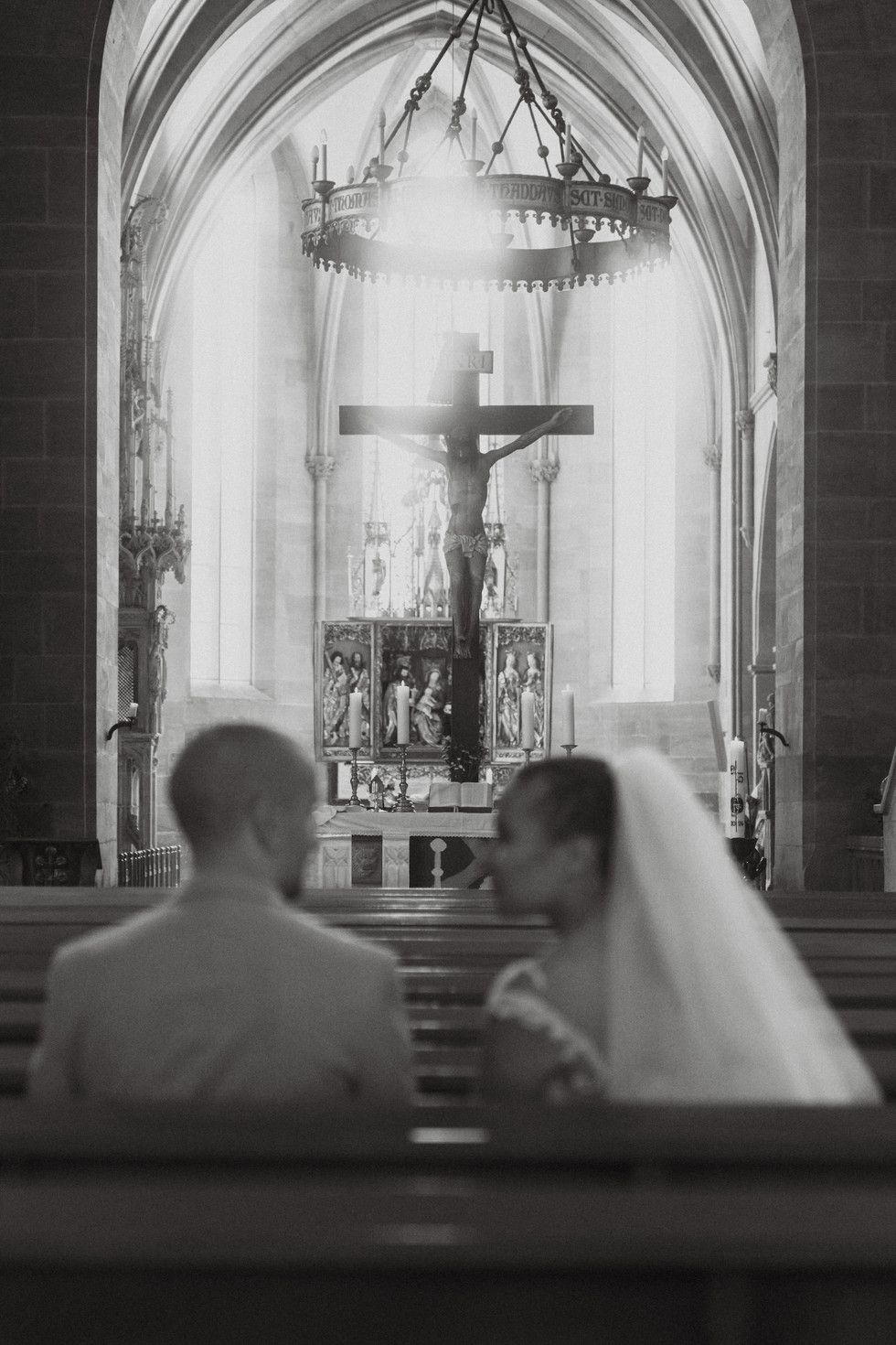 black and white shot of the bride and groom sitting in the church facing the cross with light shining through the window