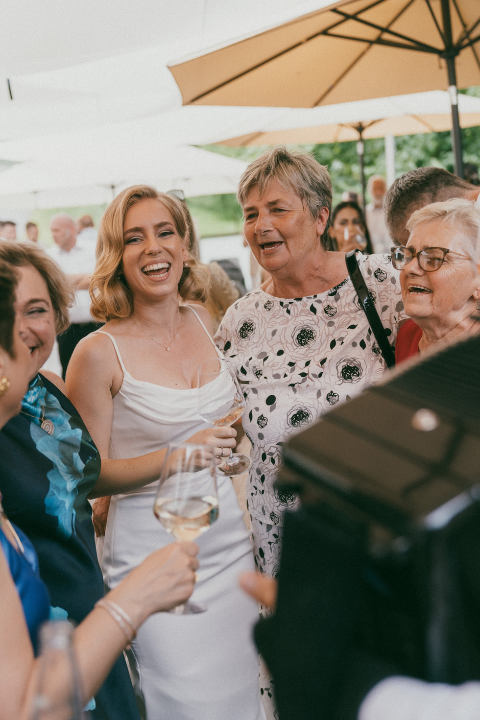bride is laughing with her family and relative while they are all holding a glass of champagne