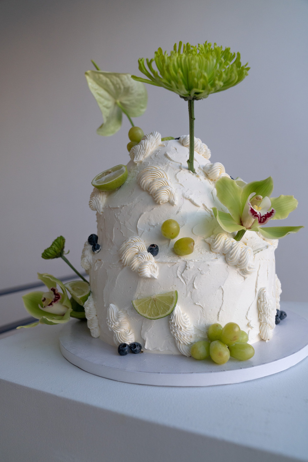 a unique, editorial wedding cake with green flowers, lime, grapes on the cake