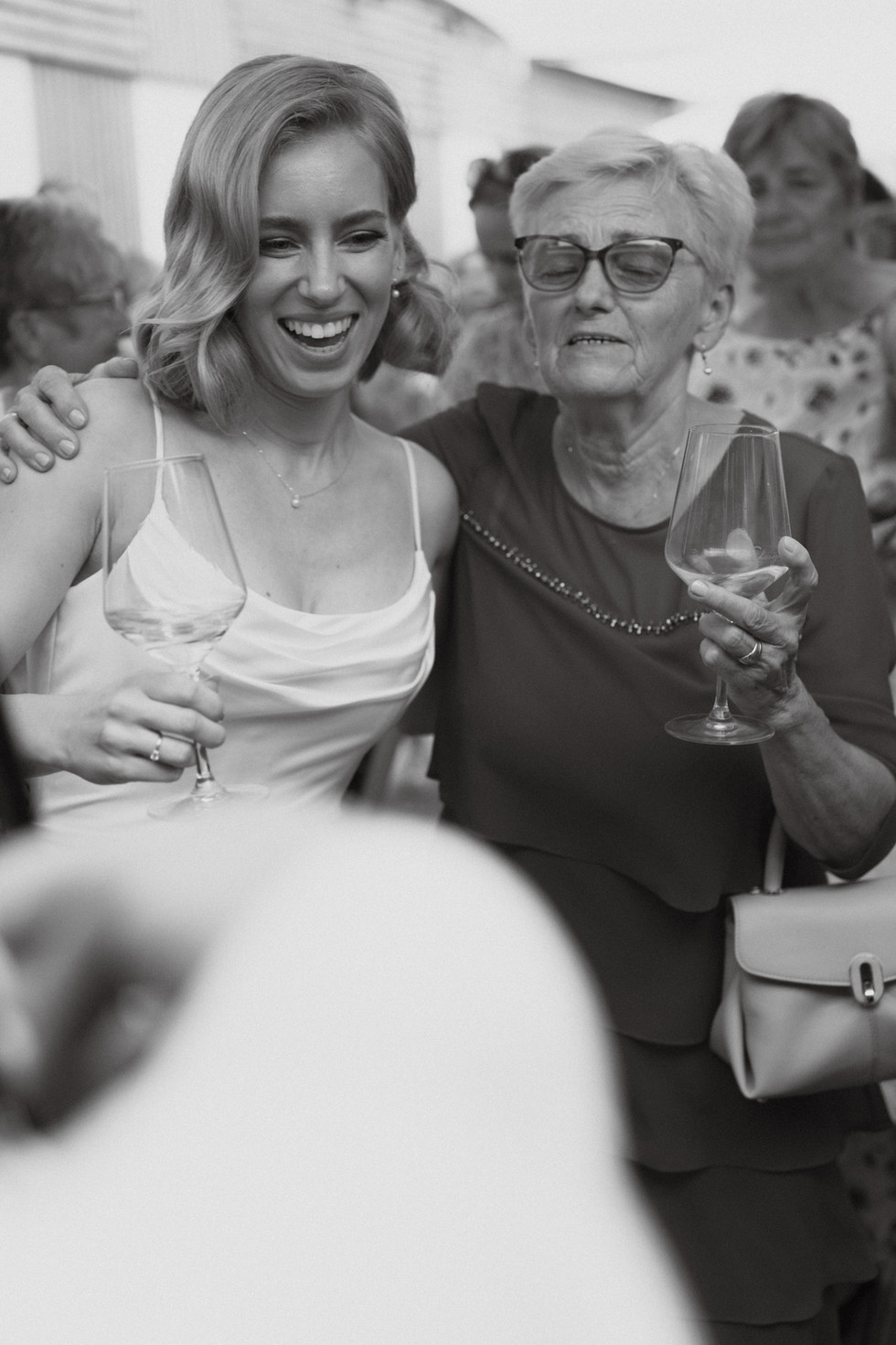 black and white photo of a precious moment of the bride and her grandmother laughing together with a class of champagne in their hands