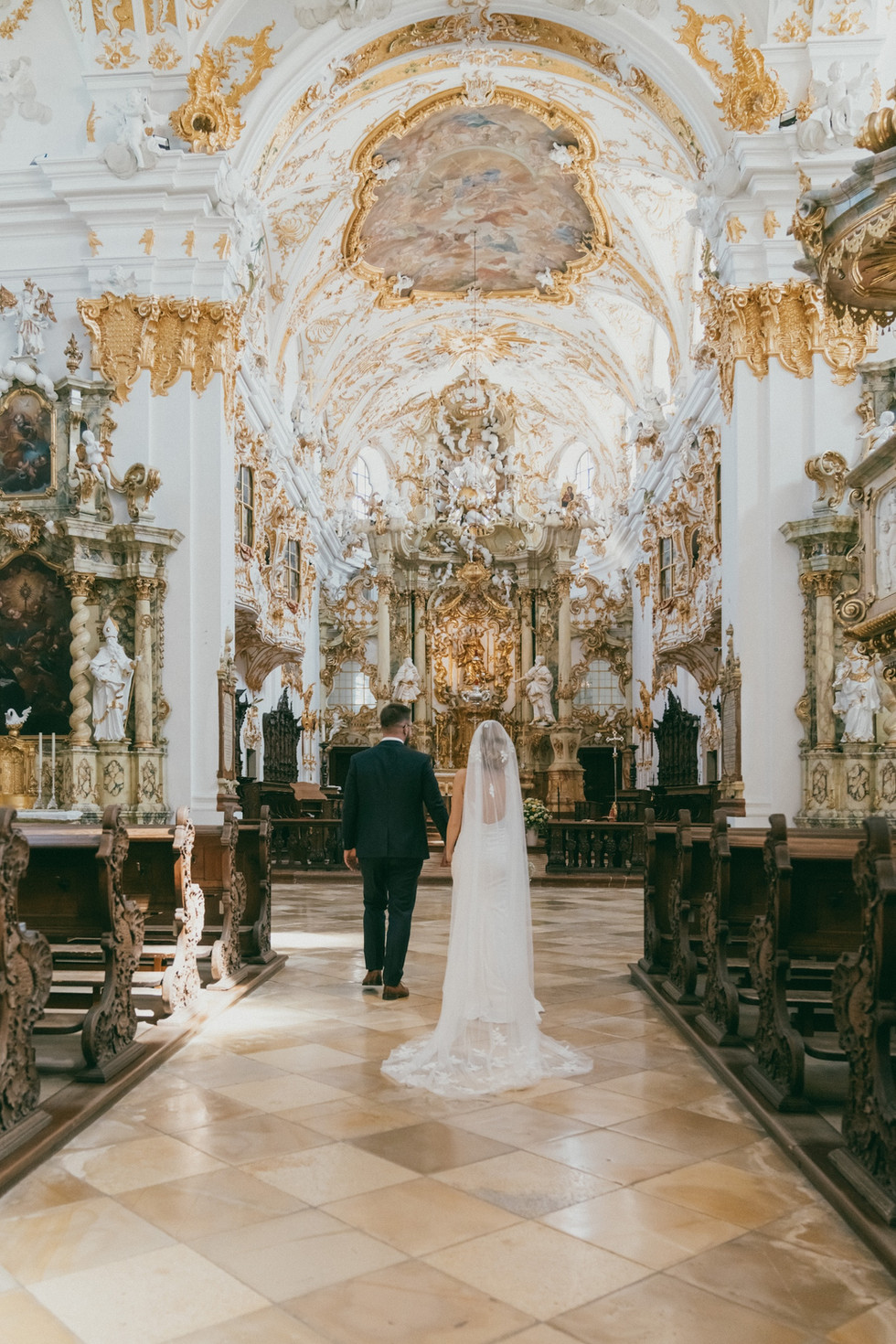 bride and groom walking down the aisle together in an extravagant golden church in regensburg germany