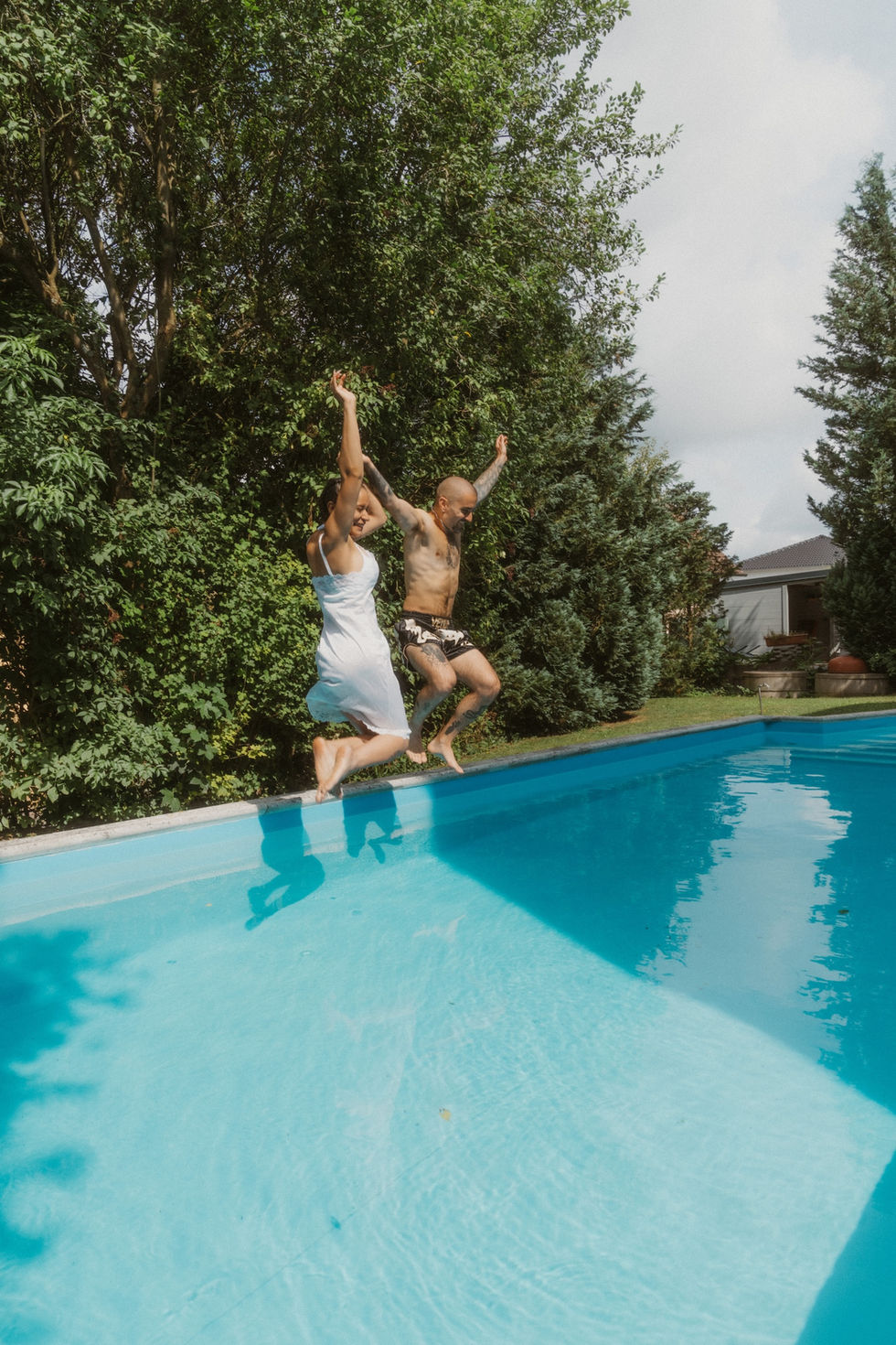 bride and groom jumping into the pool together after the wedding 