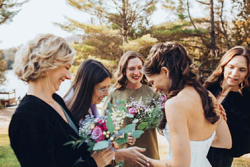 Bride with friends laughing. Woman in white dress. Wedding in nature setting.