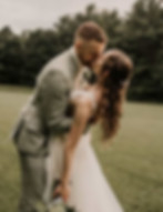 Un couple s'embrasse lors de leur mariage, robe blanche et costume gris.