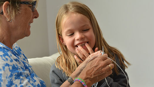A grandmother is showing her smilling granddaughter how to knit.