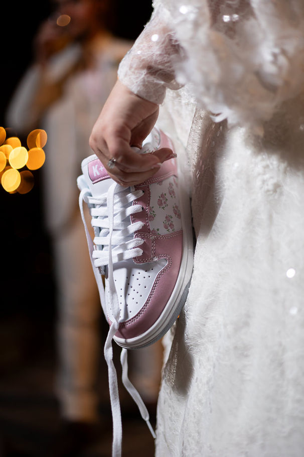 A close-up of a bride holding her custom-made white and pink Nike shoe, which she designed for going to the open dance at her wedding in Kansas City.