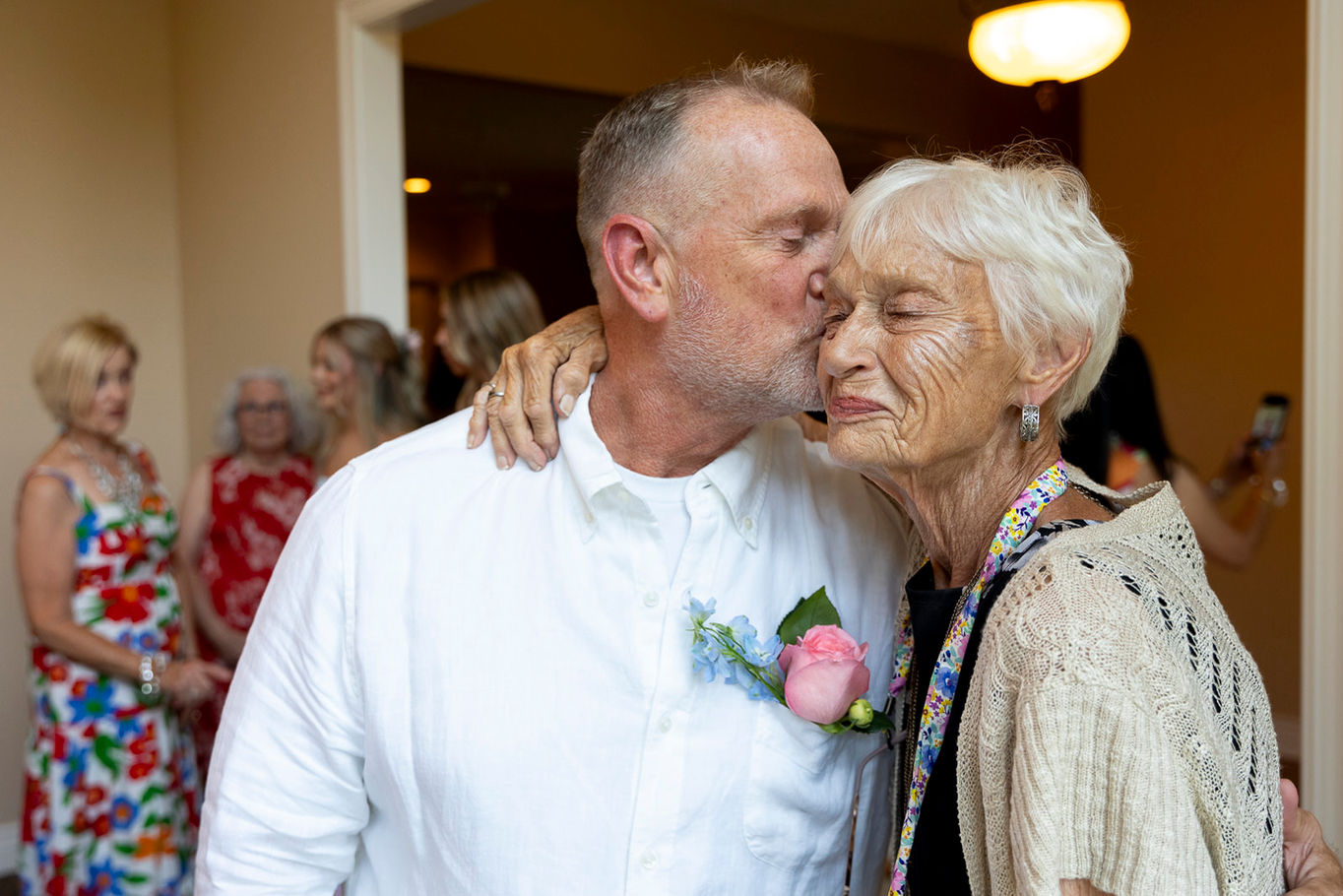 A groom in his sixties is kissing his mother on the cheek during his remarriage. His mother has a very emotional expression of love, affection, and happiness.