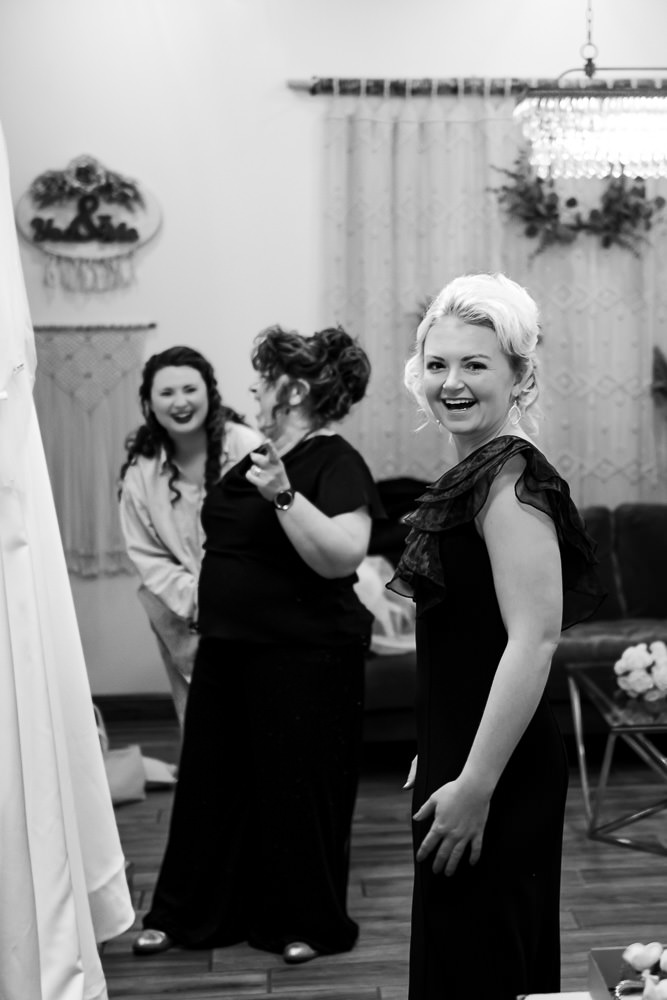 Black and white photo: Bride Tamieka, her mother, and the maid of honor share a moment of laughter, looking surprised and amused at the camera capturing their getting-ready scene.