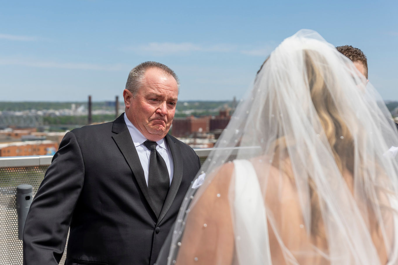 The father of the bride is seeing his daughter in her wedding dress for the first time on the rooftop of the 21C Hotel in downtown Kansas City. He is about to cry.