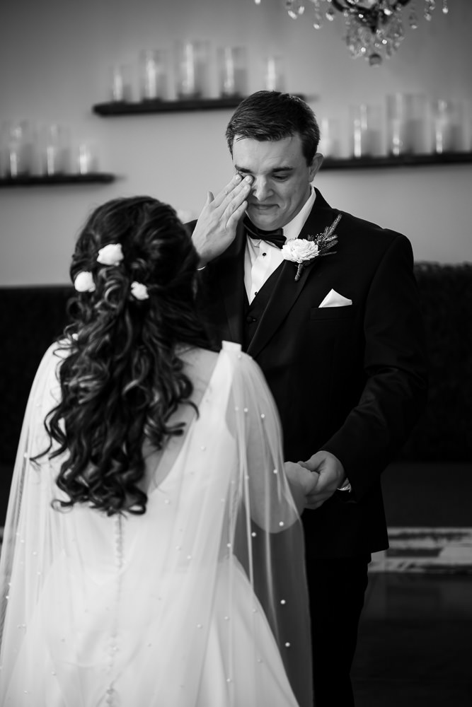 Black and white photo: Overwhelmed with emotion, groom Drake gently wipes a tear from his eye during the first look with his bride, Tamieka.