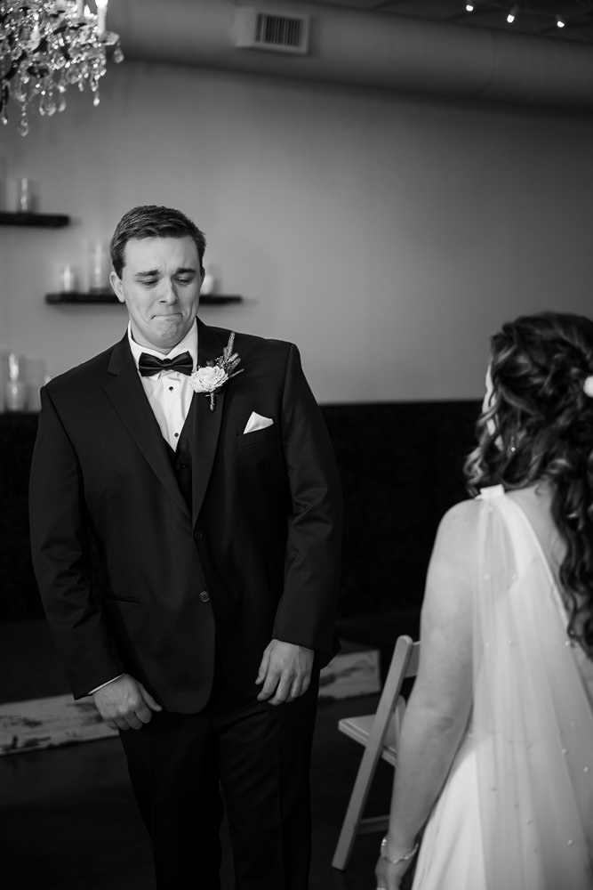 Black and white photo: In a poignant first look, groom Drake stands with tears welling in his eyes as he sees his beautiful bride for the first time.
