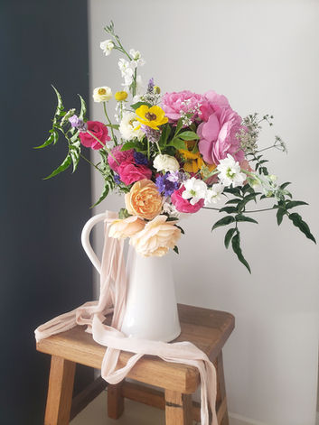 beautiful arrangement of flowers in a jug with ribbon around it
