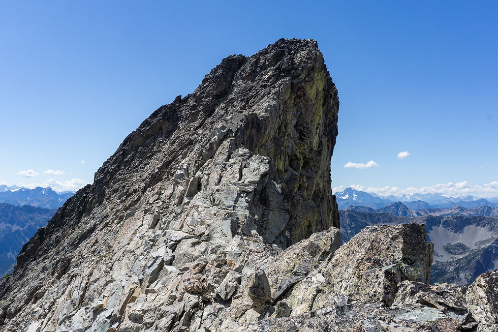 Rocky mountain peak under clear blue sky, overlooking distant snow-capped range. Rugged terrain with a sense of serenity and solitude.