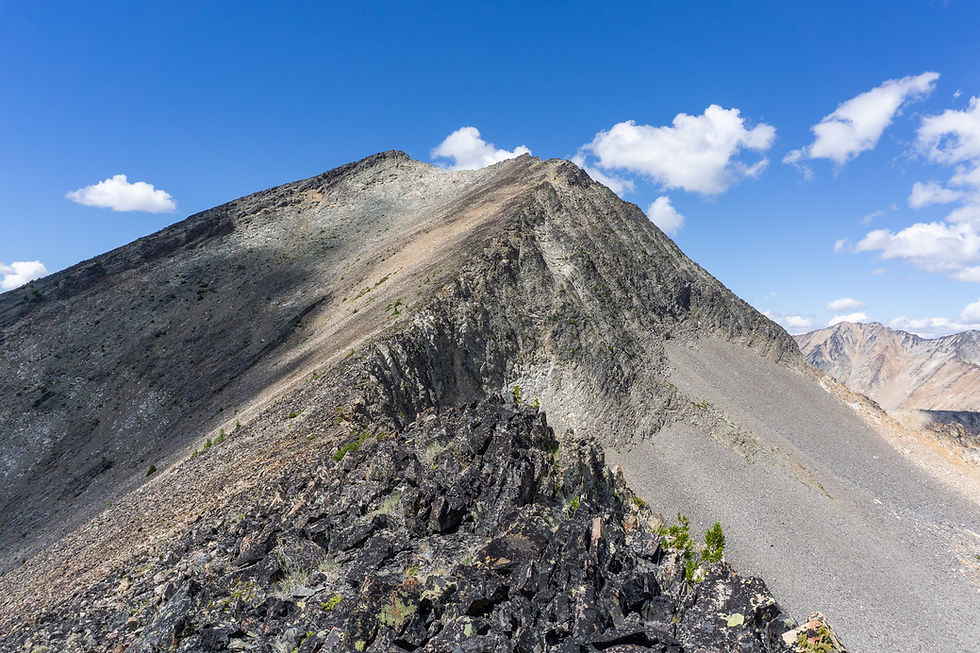 Rocky mountain peak under a clear blue sky with scattered clouds. Rugged terrain with sparse greenery conveys a tranquil, expansive mood.