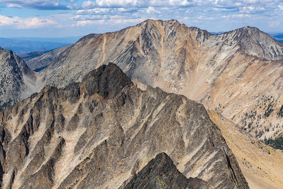 Rocky mountain landscape with rugged peaks and ridges under a partly cloudy sky.