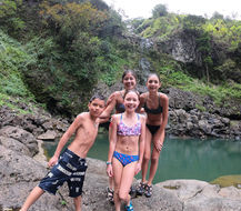 Mother with her children standing on lava rock beds in front of a large freshwater pool
