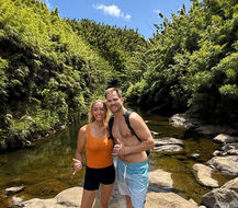 Two hikers standing on lava rock boulders in Na'ili'ilihaele Stream, with bamboo forest in the backdrop