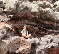 Low-Angle shot of a man meditating on a multi colored lava rock wall on the West Maui mountain loop