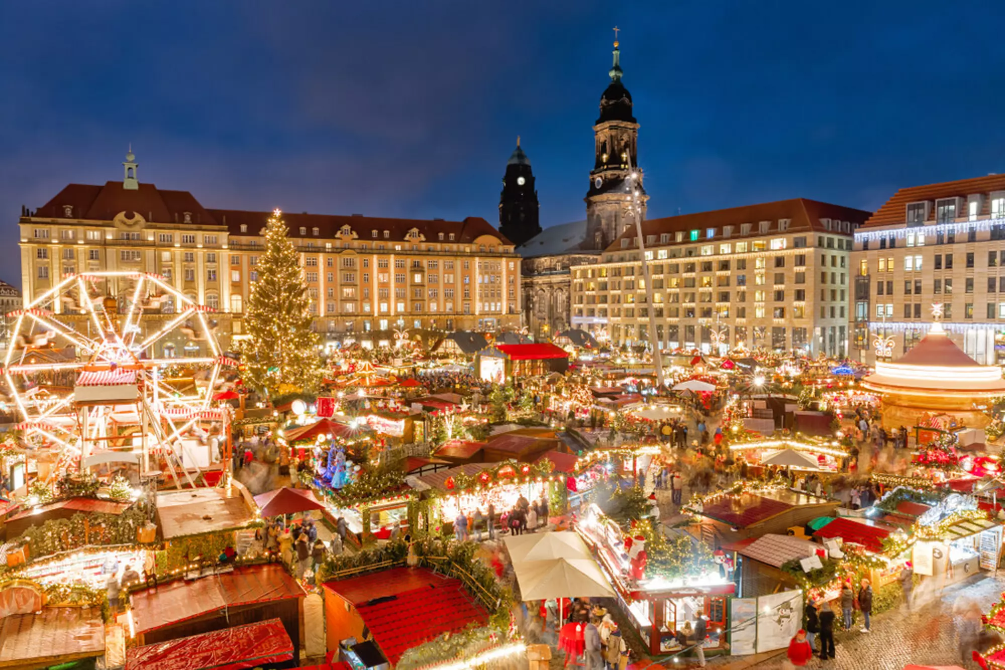 Striezelmarkt Christmas market in Dresden, Germany, illuminated at night with a Ferris wheel, festive booths, and a large Christmas tree, representing Western family-oriented celebrations.
