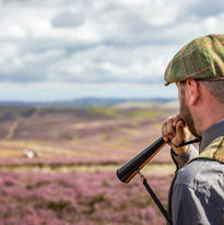 Man in cap blowing call on heather moor Walking Gun Photography image of Grouse shooting Hughes & Co