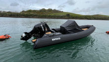 Used ribs for sale - a Black BRIG Eagle 6.7 Custom inflatable boat with Suzuki motor floats on calm water, tied to orange buoys. Green hills and cloudy sky in the background.