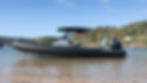 Black Brig boat with Suzuki engine docked on a clear, sunny beach. Lush green hills with houses in the background. Calm and serene scene. The BRIG Eagle 8.