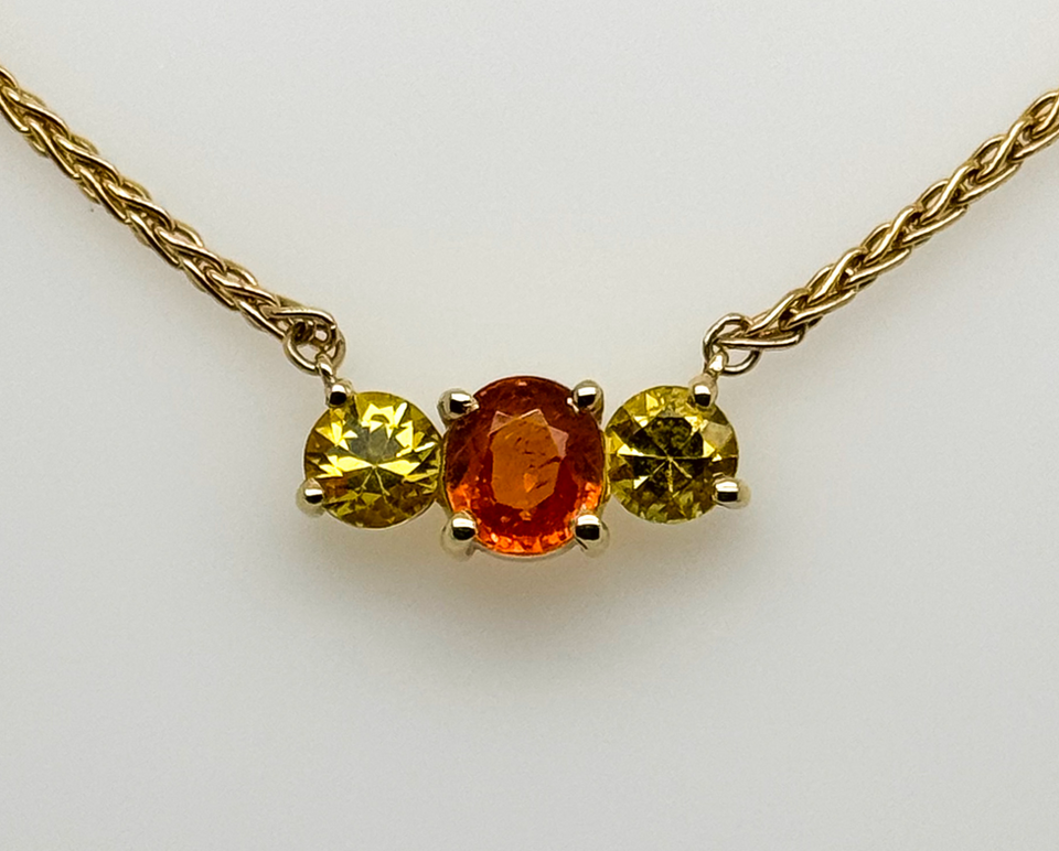 14 karat yellow gold three stone stationary pendant with a Spessartite Garnet center stone and two yellow sapphires on either side. 
