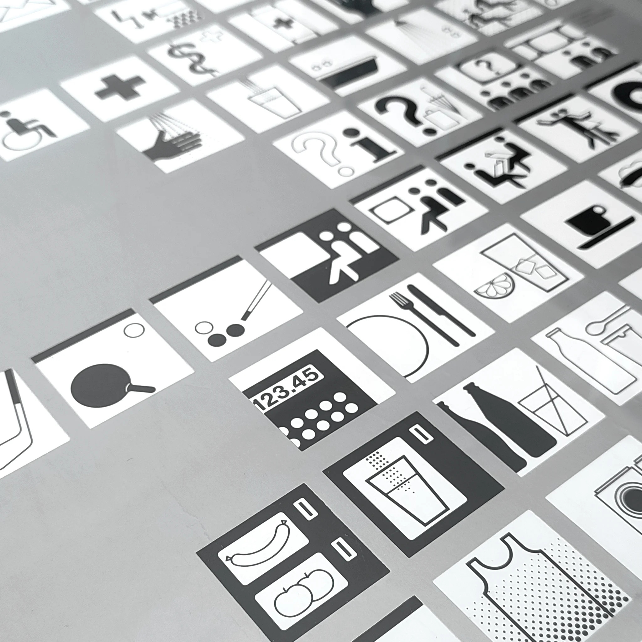 Black-and-white grid of app-style icons for food, drinks, and accessibility on a tilted screen
