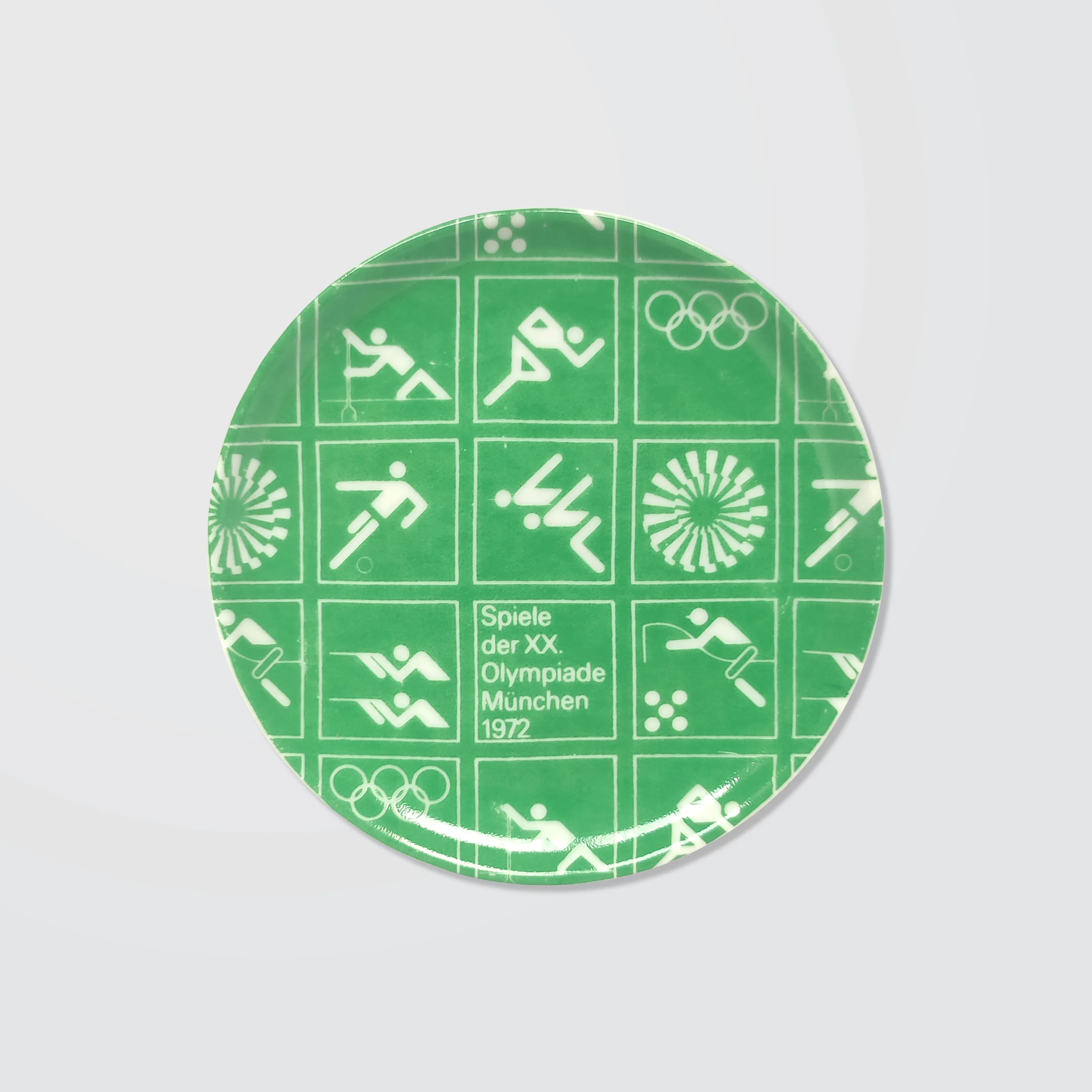 Dark green ceramic coaster with white Olympic symbols from the 1972 Munich Games, including athletic icons and "Spiele der XX. Olympiade München 1972".