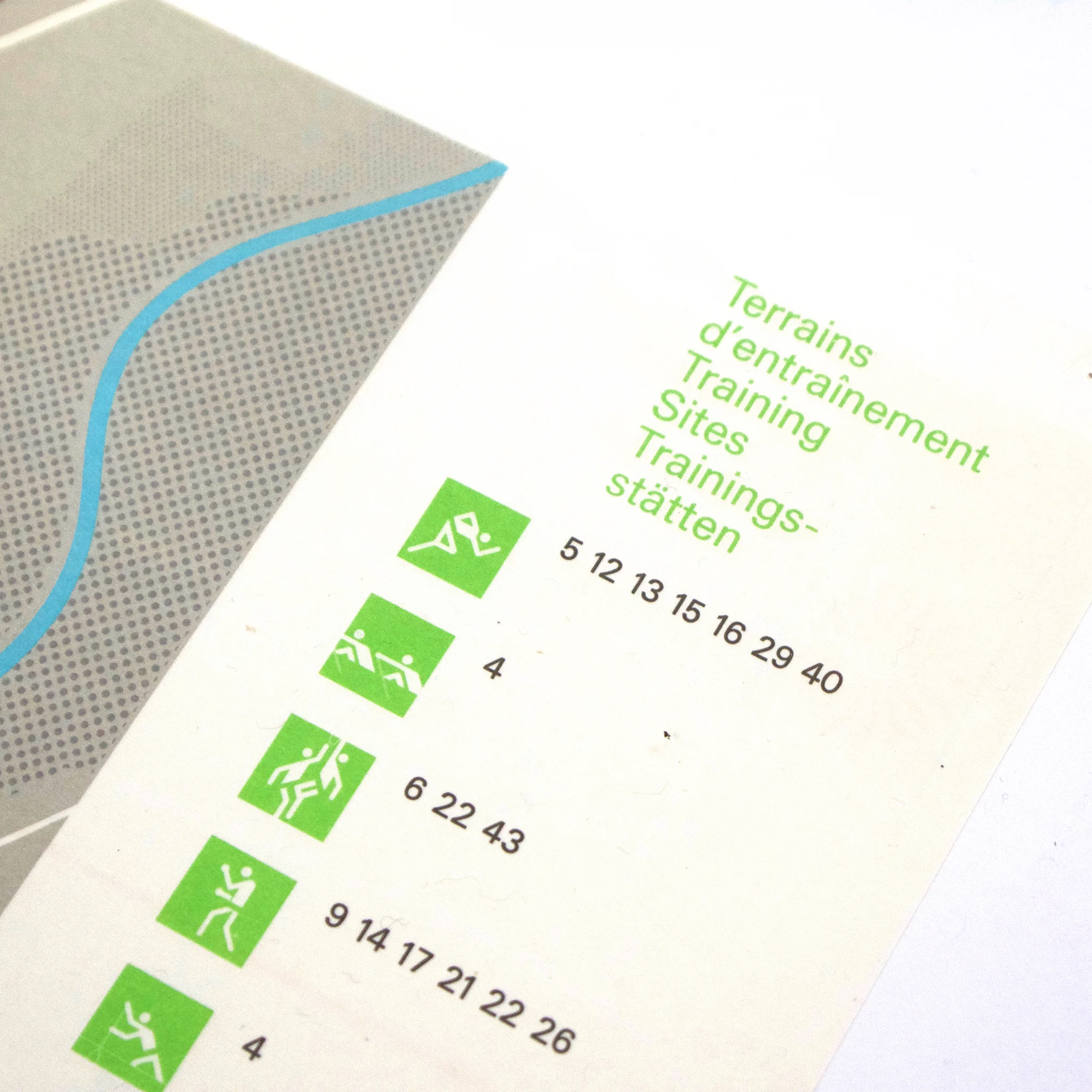Map section with green icons representing sports activities, titled "Training Sites" in three languages. Dotted grey and blue background.