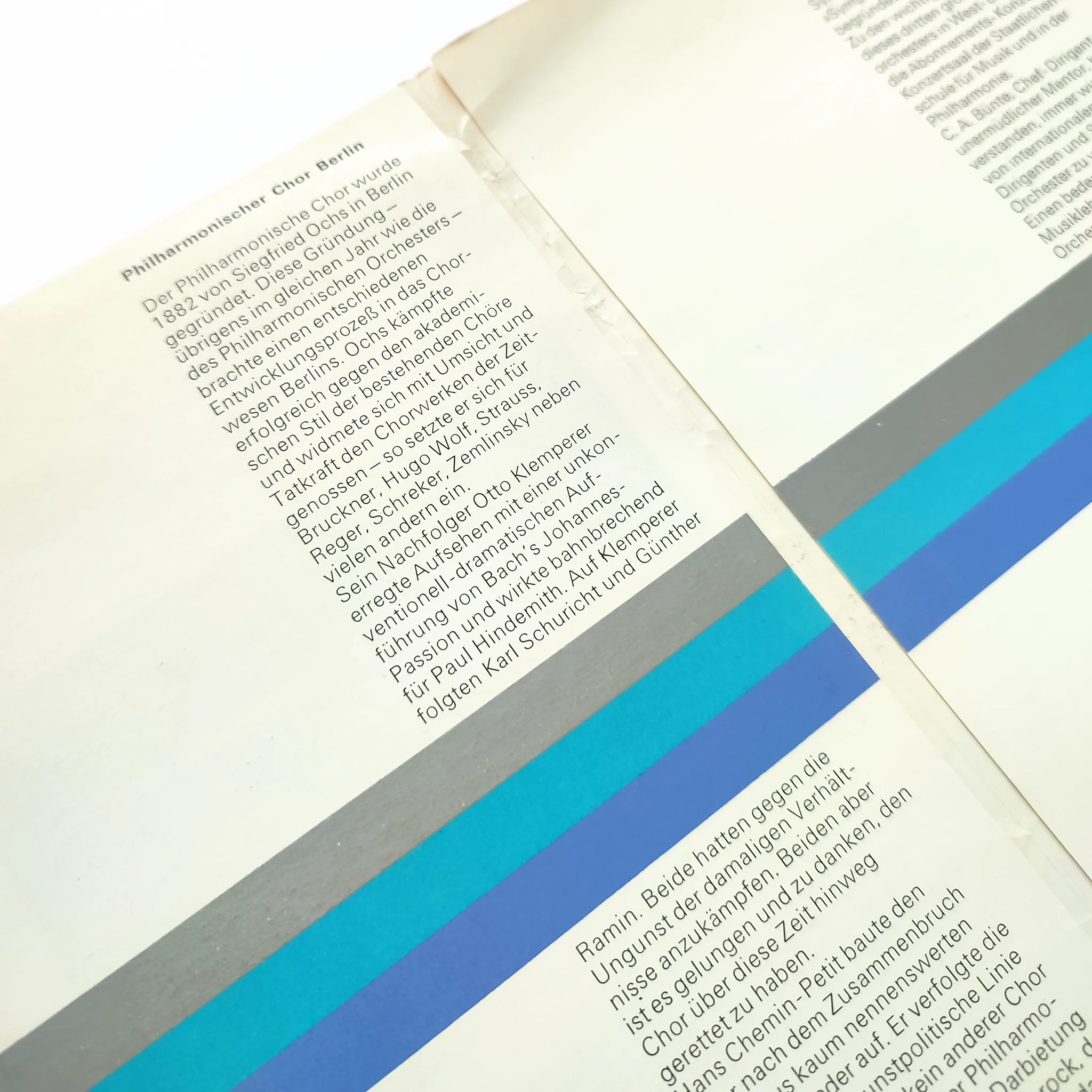 Close-up of a booklet with German text about the Philharmonic Choir Berlin. Colourful stripes in silver, light and dark blue run along the page.
