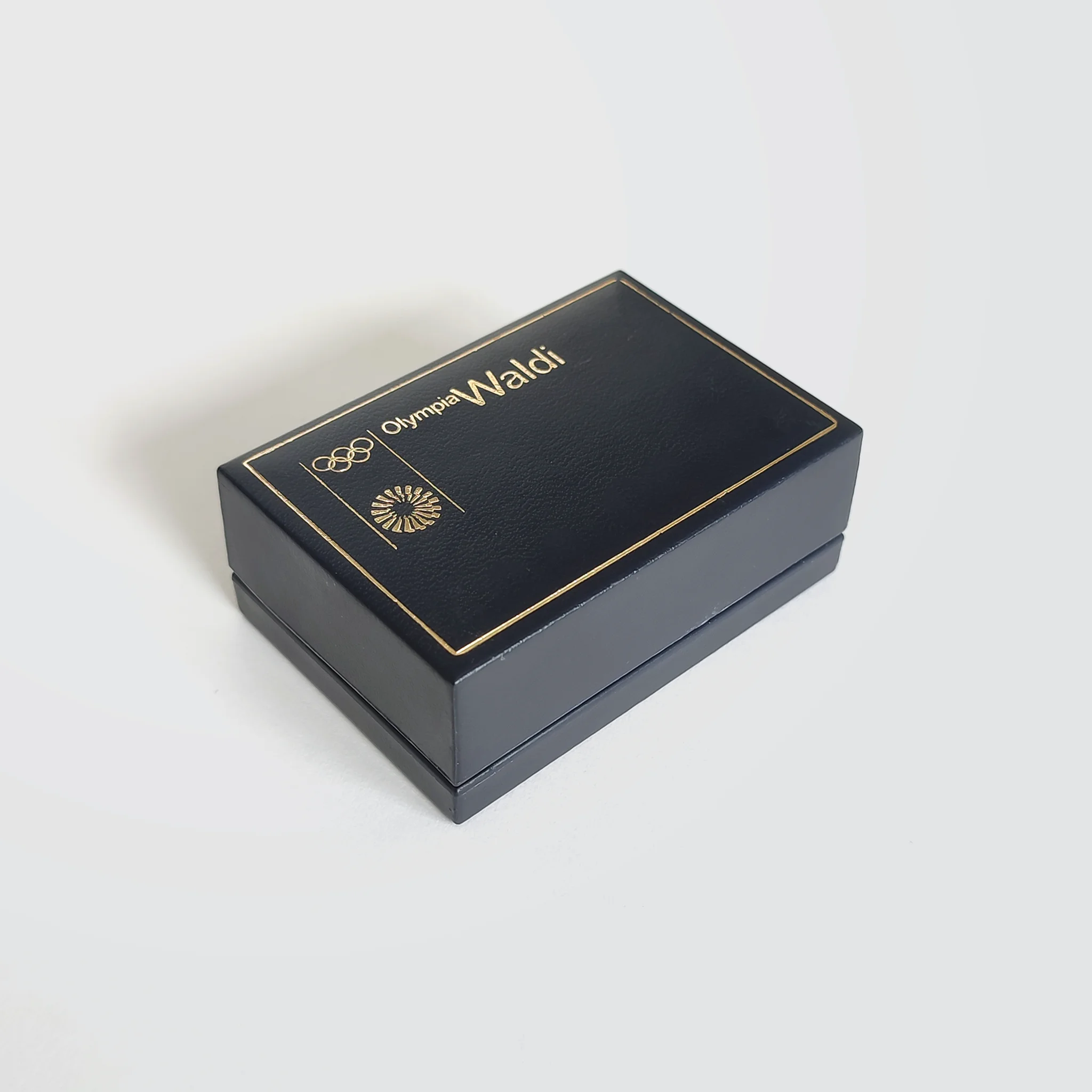 A closed jewellery box with golden Olympia Waldi text and the Olympic logos