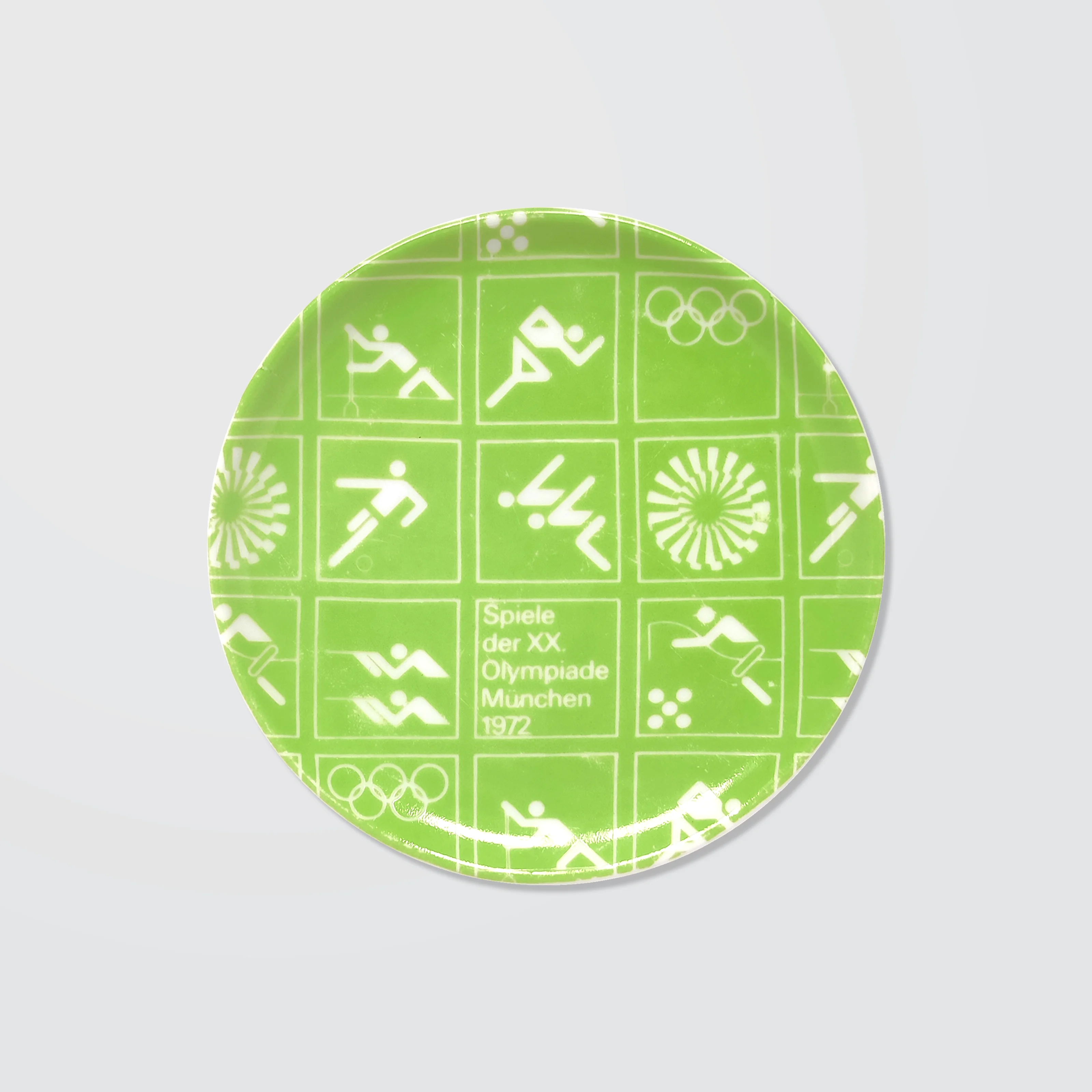Green ceramic coaster with white Olympic symbols from the 1972 Munich Games, including athletic icons and "Spiele der XX. Olympiade München 1972".