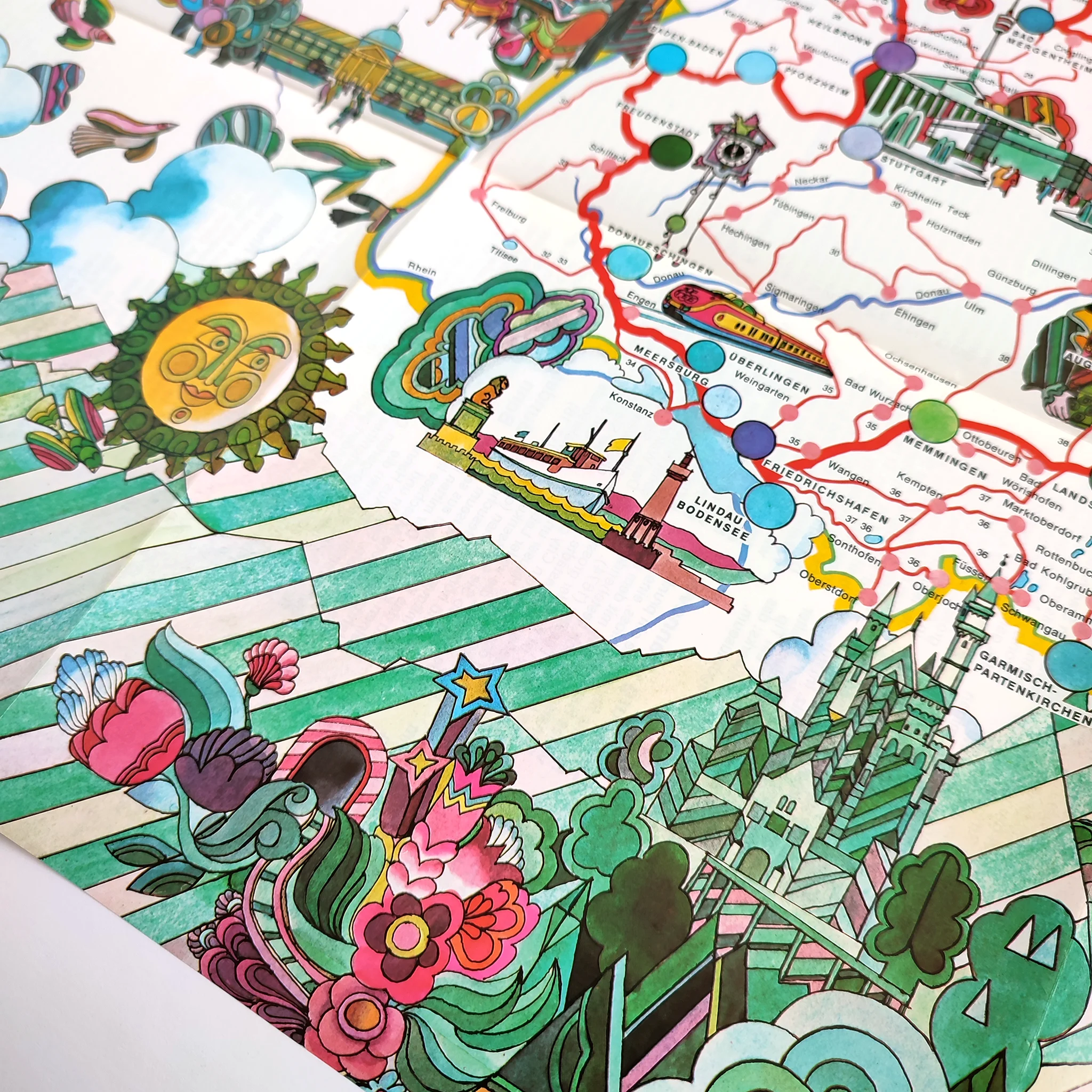 Colorful illustrated map with whimsical designs; featuring a sun, flowers, geometric patterns, and locations marked with lines and dots.