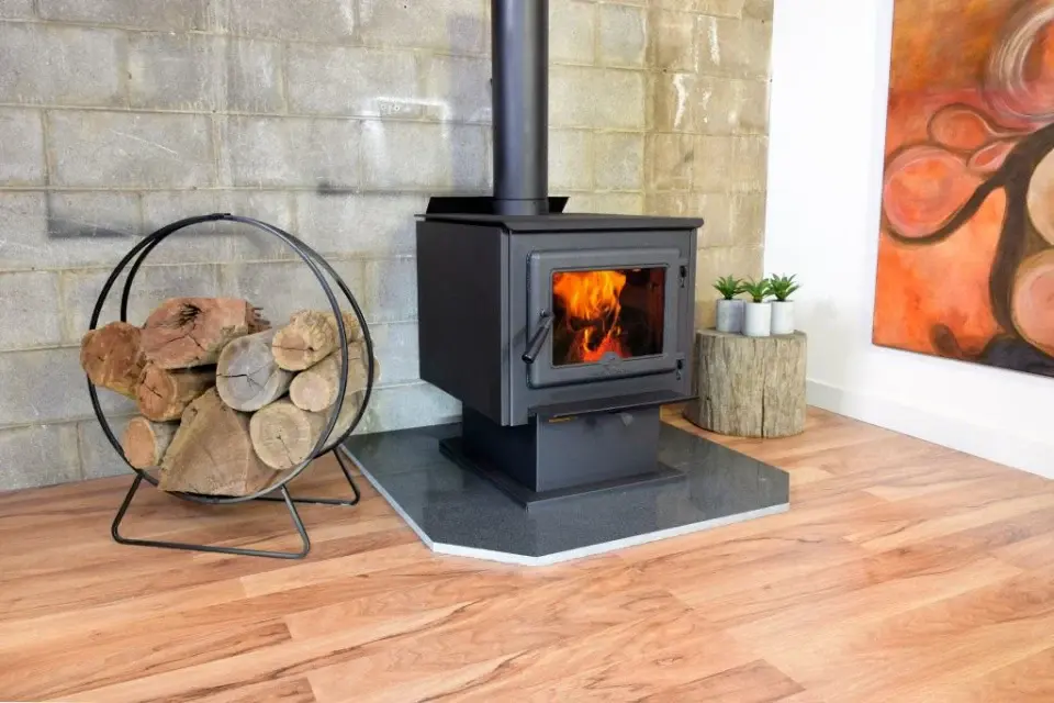 True North wood stove installed on a hearth in a home interior, with stacked firewood and a simple, functional heating setup