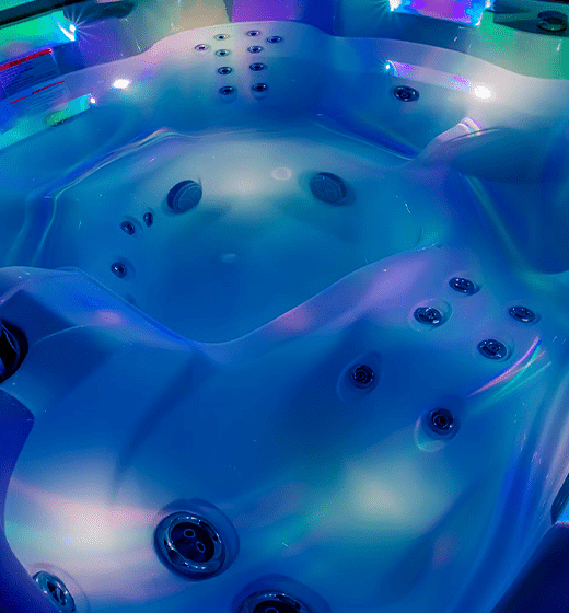 Best in Backyards' South Seas Series - 748L Deluxe Hot Tub lit up with different colors at nighttime.