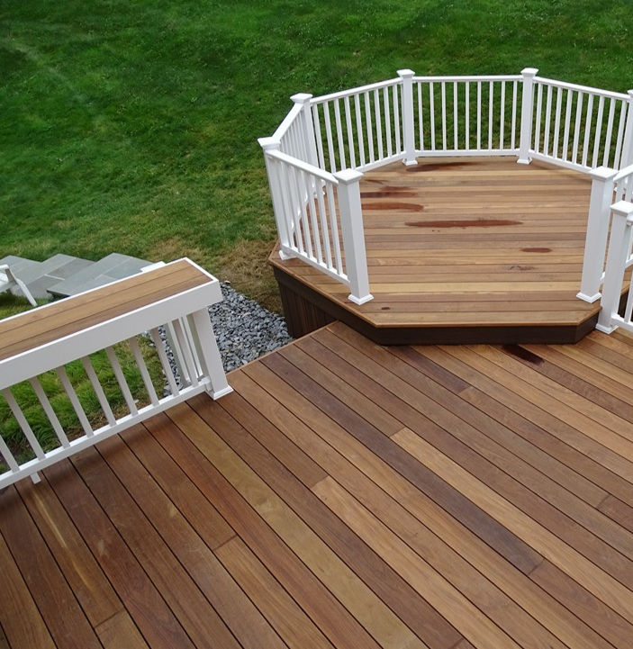 Wood deck with white railing and octagonal platform in a backyard.