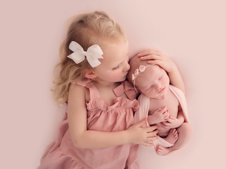 A sibling kissing her newborn sister during a photoshoot in a brighton studio