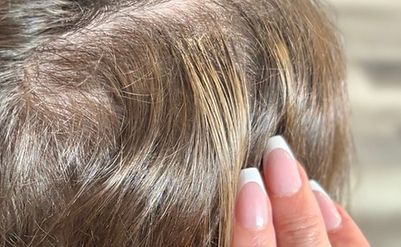 Hand touching hair with french manicure nails, close up view of the scalp.