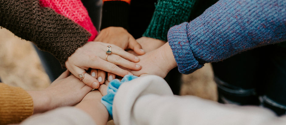 A circle of women putting their hands in the center of the circle, one on top of the other