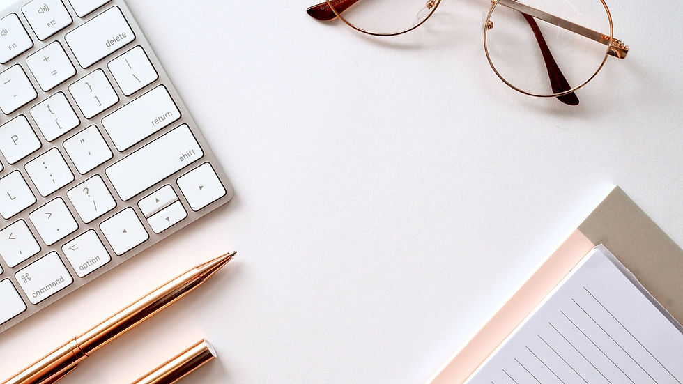 A clean workspace with anotepad, keyboard, glasses, and a pen