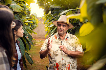 Homem de chapéu falando a um grupo em plantação